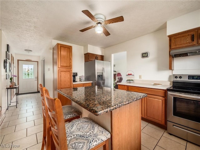 kitchen featuring a textured ceiling, appliances with stainless steel finishes, a breakfast bar, under cabinet range hood, and light tile patterned flooring