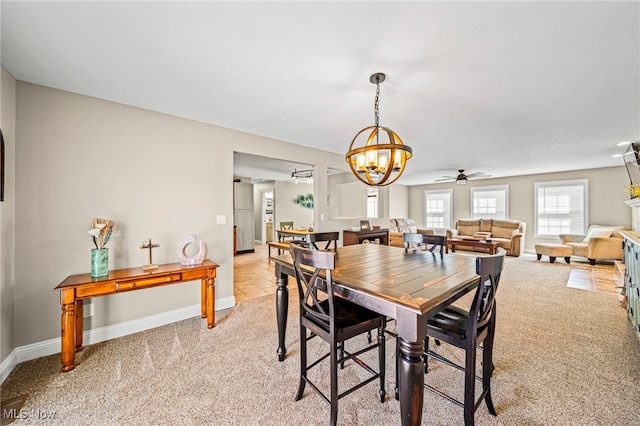 dining area featuring light colored carpet, baseboards, and ceiling fan with notable chandelier