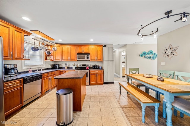 kitchen featuring a kitchen island, dark countertops, appliances with stainless steel finishes, brown cabinets, and light tile patterned floors