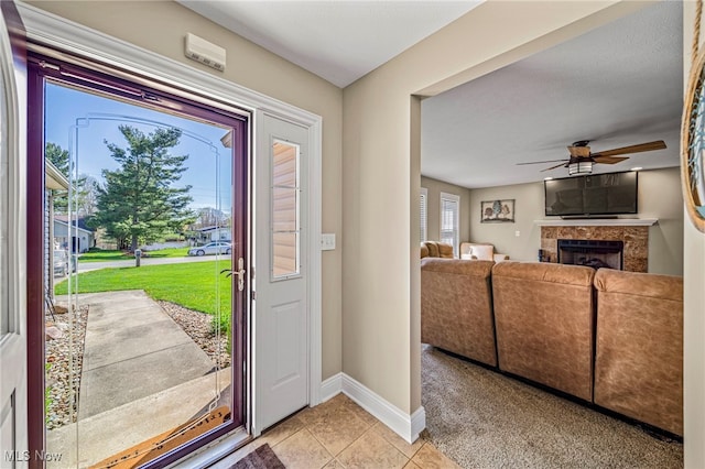 entryway featuring light tile patterned flooring, ceiling fan, light colored carpet, baseboards, and a tile fireplace