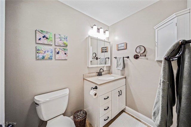 half bathroom with toilet, baseboards, and vanity