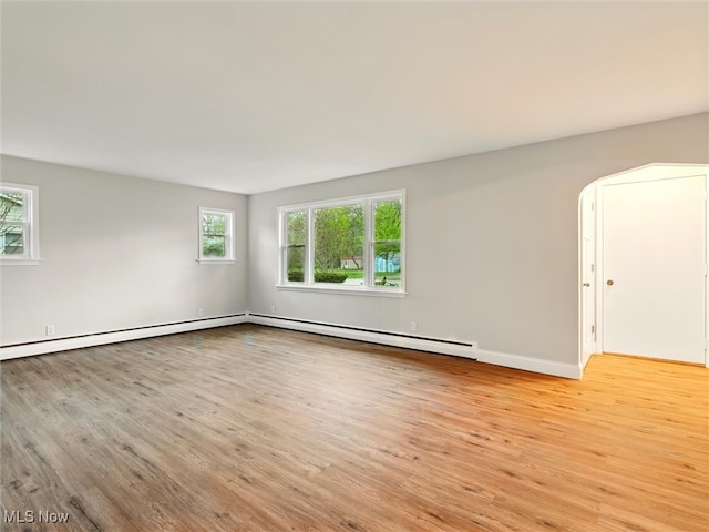 unfurnished room featuring baseboards, baseboard heating, arched walkways, and light wood-style flooring