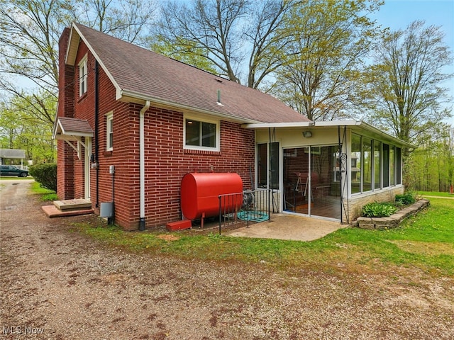 rear view of house featuring a sunroom, roof with shingles, heating fuel, and brick siding