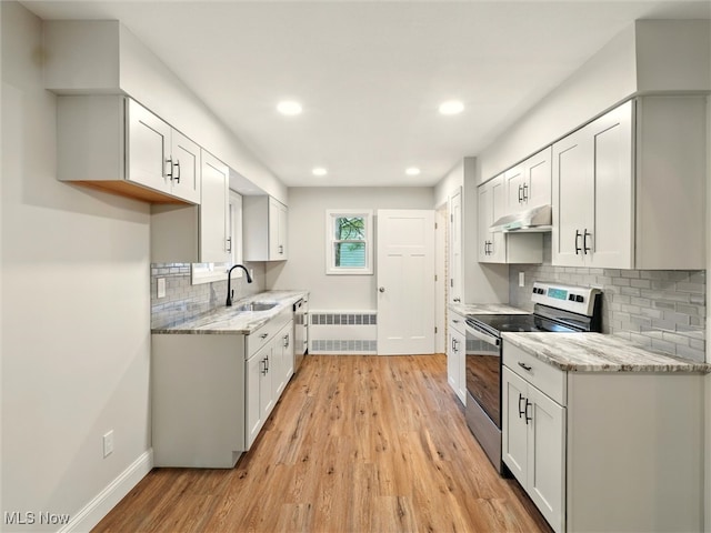 kitchen featuring stainless steel electric range oven, a sink, radiator heating unit, under cabinet range hood, and light wood-style flooring
