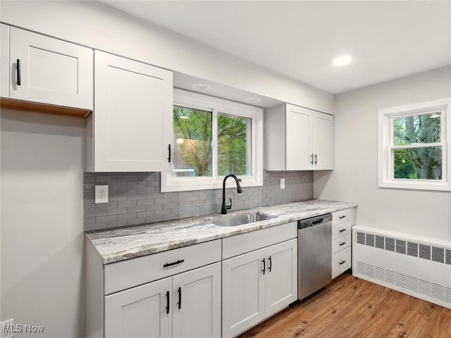 kitchen with stainless steel dishwasher, radiator, white cabinets, tasteful backsplash, and a sink
