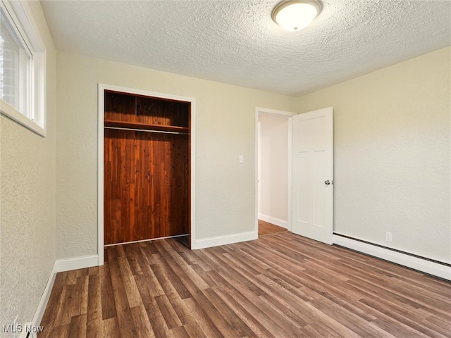 unfurnished bedroom featuring baseboards, a textured wall, a closet, and wood finished floors