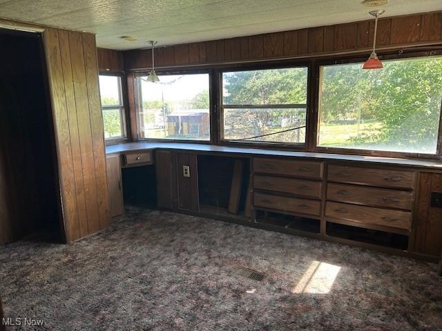 kitchen with carpet flooring, wooden walls, and pendant lighting