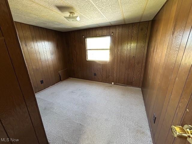 unfurnished room with light colored carpet and wood walls