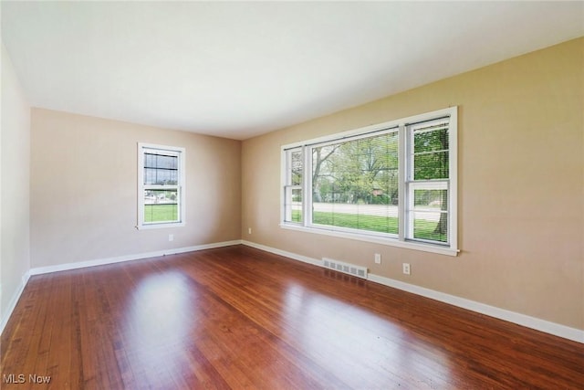 empty room featuring visible vents, dark wood-style floors, and a wealth of natural light