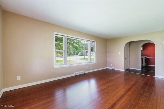 empty room with arched walkways, baseboards, wood finished floors, and visible vents