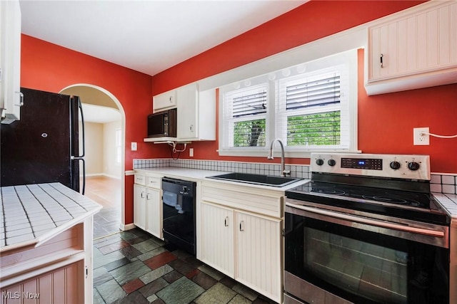 kitchen featuring a sink, light countertops, arched walkways, black appliances, and stone tile flooring