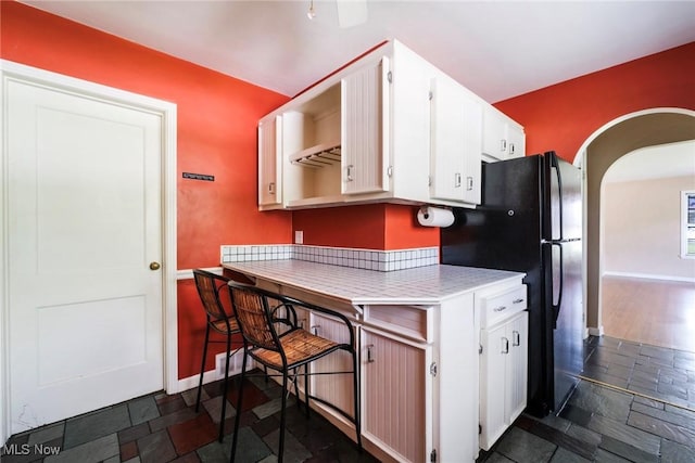 kitchen with light countertops, arched walkways, white cabinetry, and stone tile floors