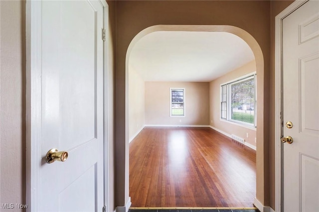 interior space with arched walkways, baseboards, visible vents, and wood finished floors