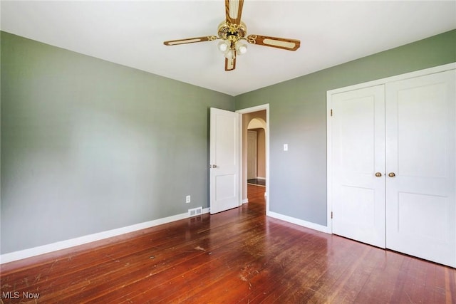 unfurnished bedroom featuring visible vents, a closet, wood-type flooring, baseboards, and arched walkways