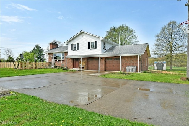 tri-level home with fence, an attached garage, a front lawn, brick siding, and driveway