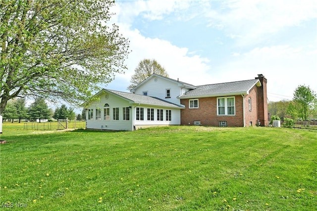 rear view of house featuring fence, a chimney, a yard, and brick siding
