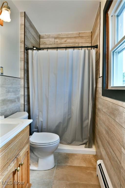 full bath with a stall shower, wood walls, vanity, a baseboard heating unit, and toilet