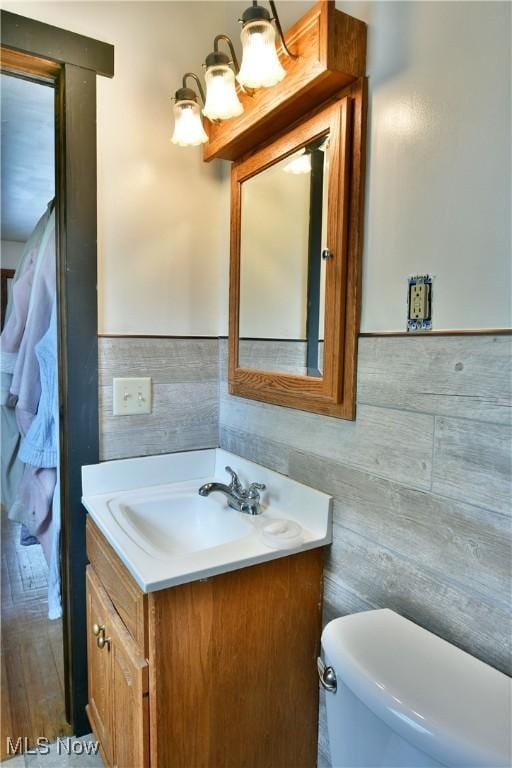 half bath with vanity, a wainscoted wall, toilet, and tile walls