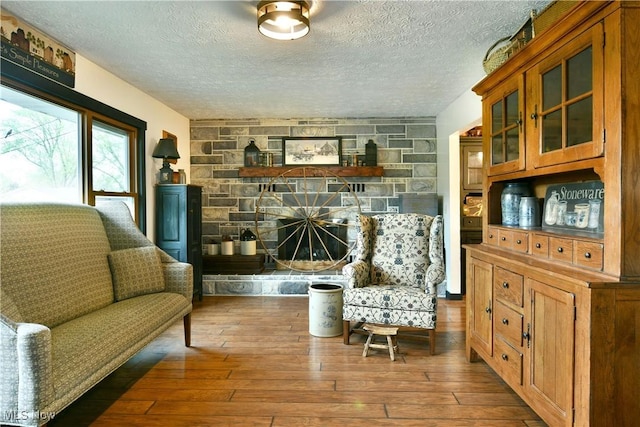 living area featuring a stone fireplace, hardwood / wood-style flooring, and a textured ceiling