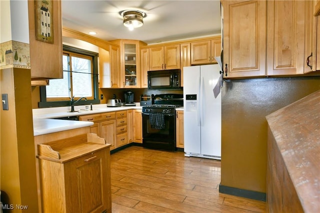 kitchen with a sink, light countertops, light wood-type flooring, glass insert cabinets, and black appliances