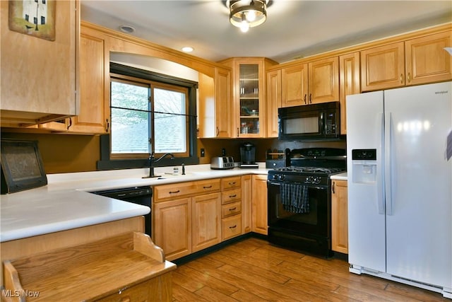 kitchen featuring wood finished floors, a sink, light countertops, black appliances, and glass insert cabinets