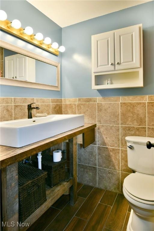 bathroom featuring wainscoting, toilet, tile walls, wood finish floors, and a sink