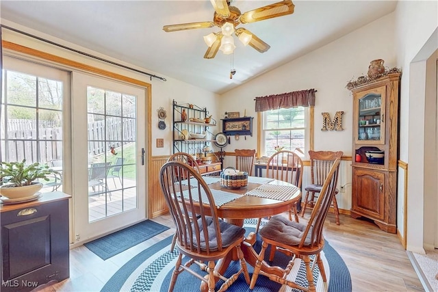 dining space featuring light wood-style flooring, ceiling fan, a wainscoted wall, and vaulted ceiling
