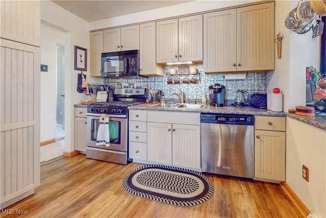 kitchen with baseboards, light wood-type flooring, a sink, backsplash, and stainless steel appliances