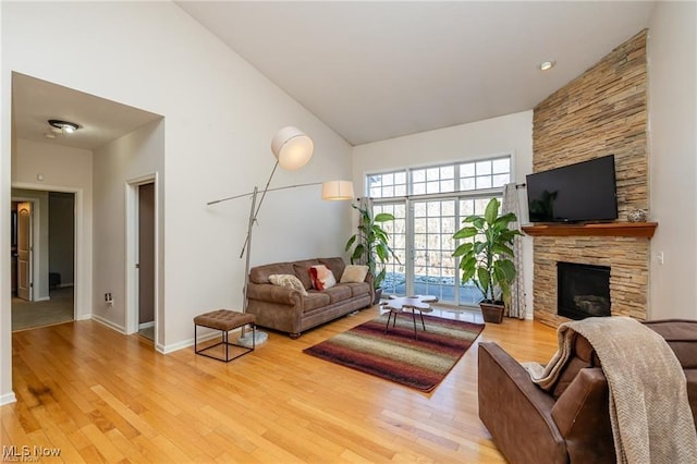 living area with baseboards, high vaulted ceiling, light wood-type flooring, and a stone fireplace