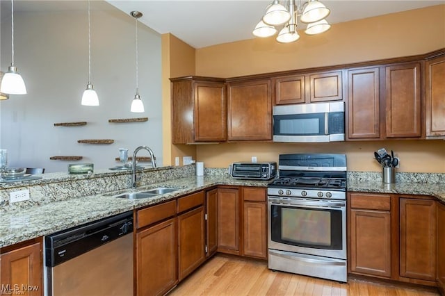 kitchen with appliances with stainless steel finishes, light stone countertops, a sink, light wood finished floors, and a chandelier