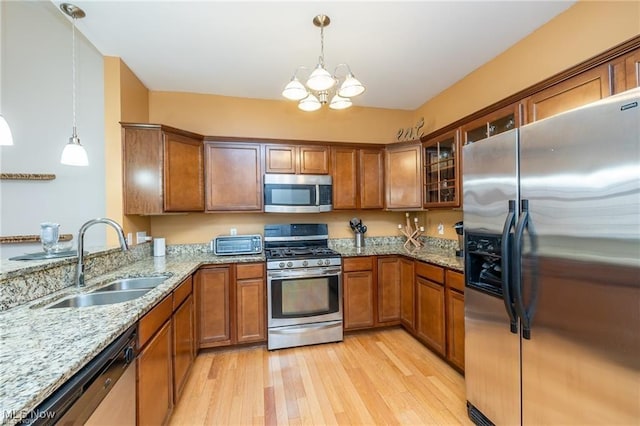 kitchen featuring brown cabinetry, light wood-style floors, a chandelier, a sink, and appliances with stainless steel finishes