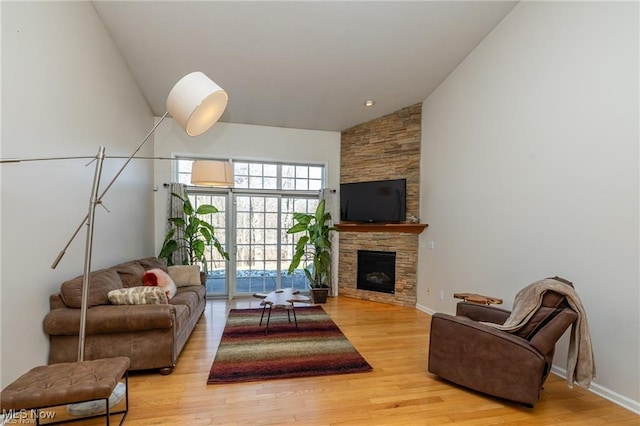 living room featuring baseboards, high vaulted ceiling, a stone fireplace, and light wood-style flooring
