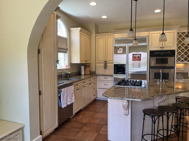 kitchen with a kitchen breakfast bar, recessed lighting, cream cabinets, arched walkways, and appliances with stainless steel finishes