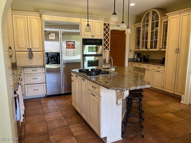 kitchen with appliances with stainless steel finishes, a kitchen island with sink, cream cabinetry, and a kitchen bar