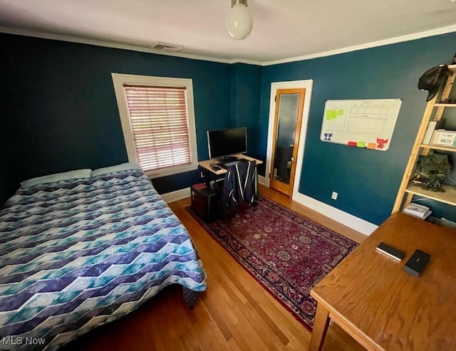 bedroom with baseboards, visible vents, ornamental molding, and wood finished floors