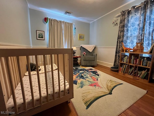 bedroom with visible vents, ornamental molding, baseboards, and wood finished floors