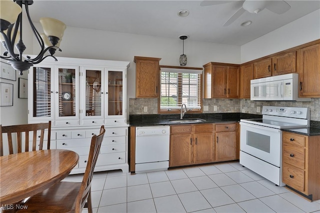 kitchen with decorative backsplash, brown cabinetry, dark countertops, a sink, and white appliances