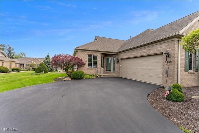 ranch-style home with a garage, aphalt driveway, a front yard, roof with shingles, and brick siding