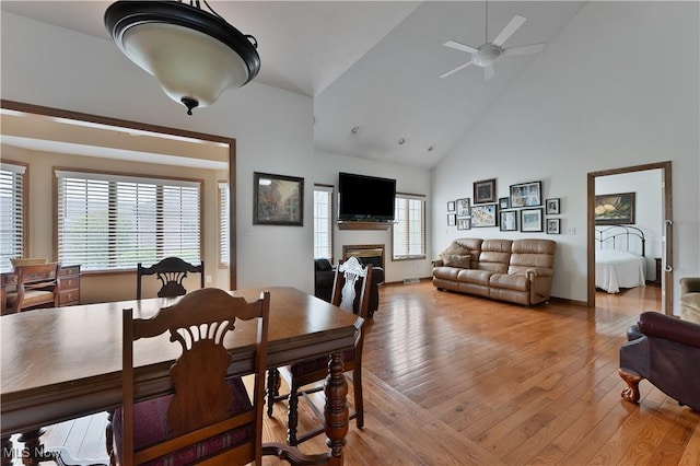 dining room featuring high vaulted ceiling, ceiling fan, a fireplace, and wood-type flooring