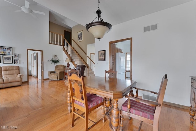dining space featuring light wood-style floors, a ceiling fan, a towering ceiling, visible vents, and stairway