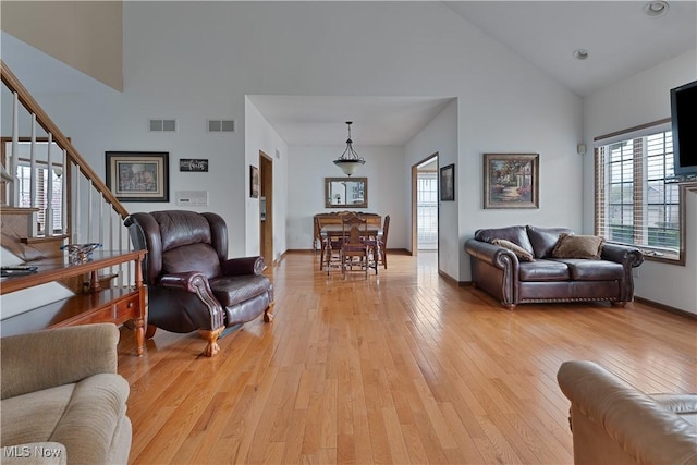 living area with high vaulted ceiling, visible vents, and light wood-style floors