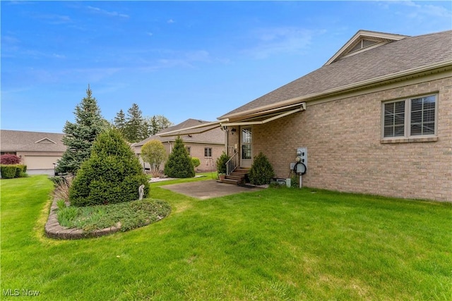 rear view of house with a yard, brick siding, a shingled roof, and entry steps