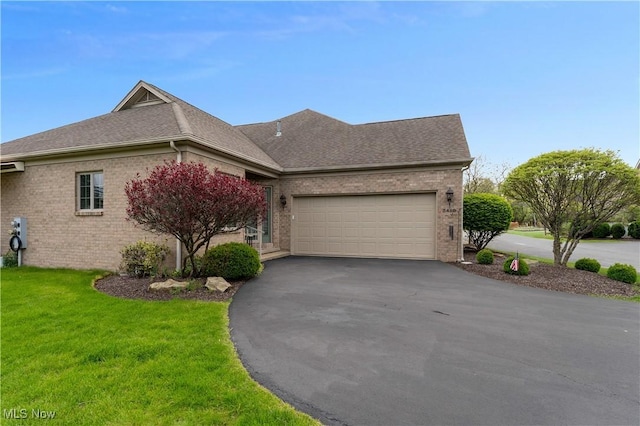 ranch-style home featuring a front yard, roof with shingles, brick siding, an attached garage, and driveway