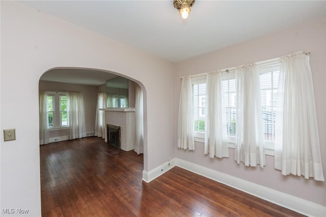 unfurnished living room with arched walkways, baseboards, dark wood finished floors, and a fireplace