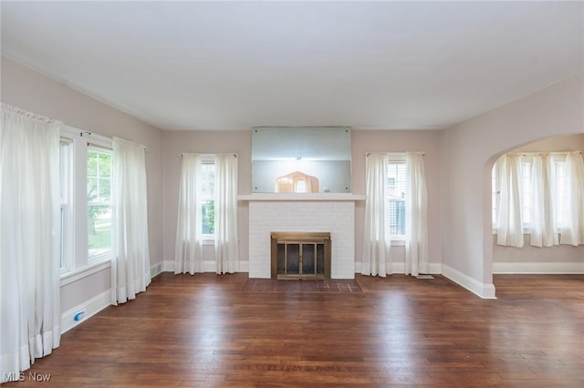 unfurnished living room with arched walkways, baseboards, a healthy amount of sunlight, and wood finished floors