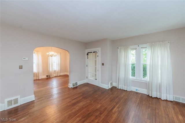 empty room featuring arched walkways, a chandelier, baseboards, visible vents, and hardwood / wood-style flooring