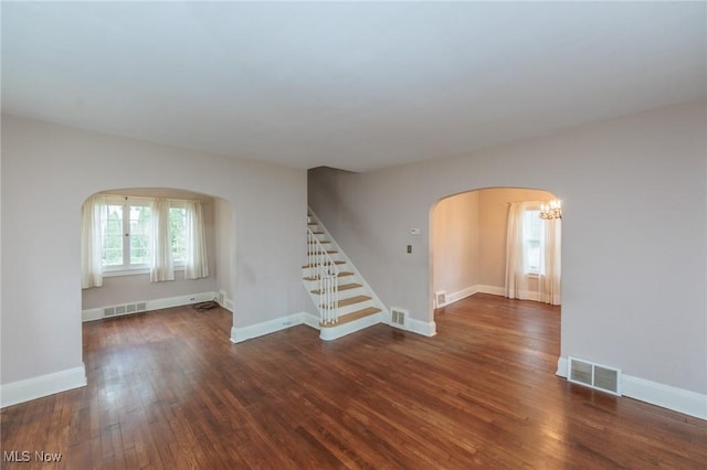 spare room featuring arched walkways, visible vents, wood finished floors, and stairway