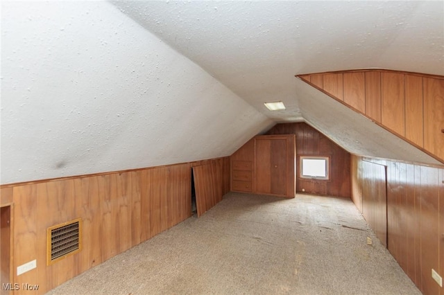 bonus room with wooden walls, vaulted ceiling, and visible vents