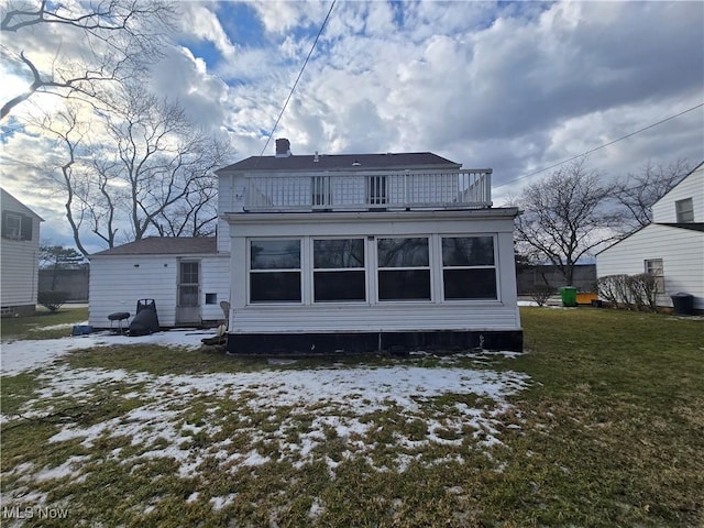 snow covered rear of property with a lawn and a balcony