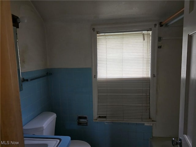 bathroom with toilet, tile walls, a wainscoted wall, and a shower